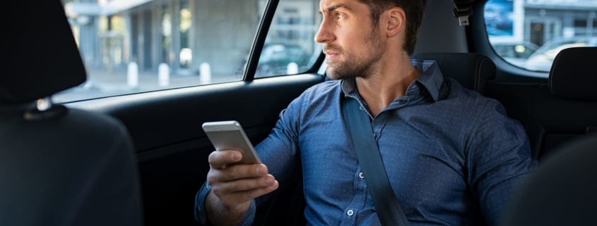 Business man is sitting in a car and using his smartphone