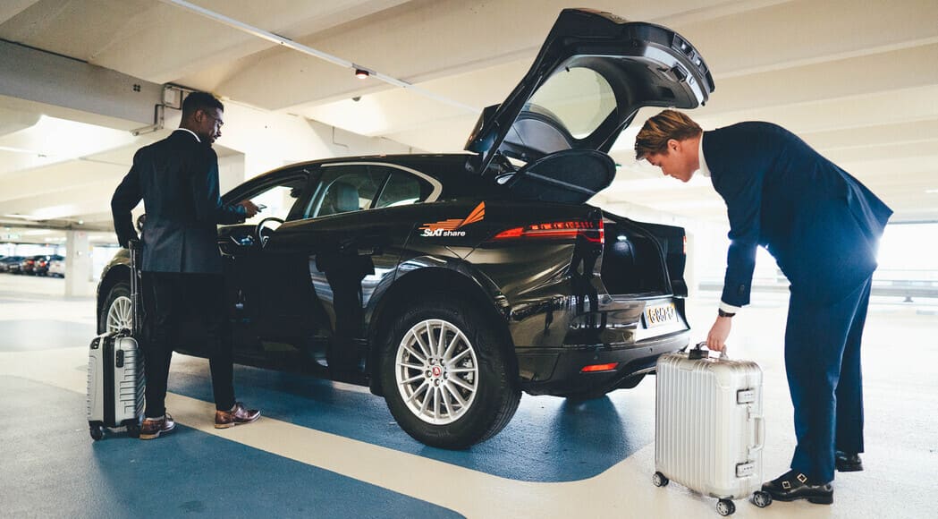 Zwei Geschäftsmänner mit Koffer nutzen Corporate Carsharing zur Buchung eines Autos