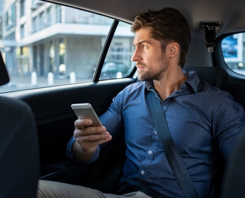 Business man is sitting in a car and using his smartphone